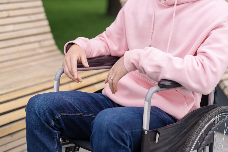 Close-up of person wearing a pink hoodie sitting in a wheelchair outside.